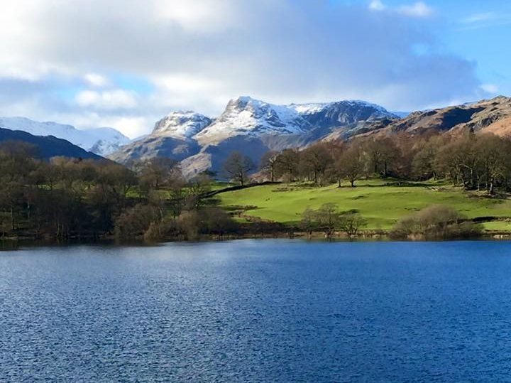 View of Loughrigg Tarn with a snow-capped peaks beyond and a blue sky